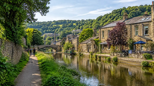 People walking beside the canal in Hebden Bridge with narrowboats, stone buildings and green hills in the background.