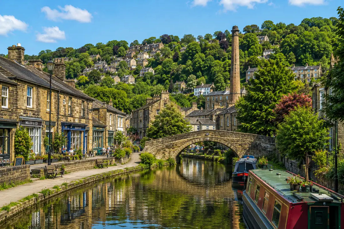Sunny view of Hebden Bridge with the Rochdale Canal, stone bridge, narrowboats and hillside buildings in West Yorkshire.