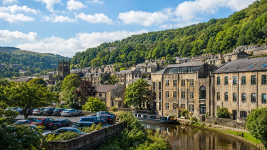 Car park beside the canal in Hebden Bridge with stone buildings, narrowboats and green hills in the background.